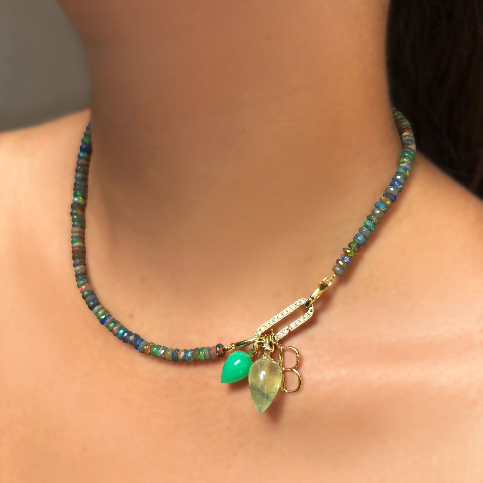 Low light faceted opal necklace with Full Pave Slim Oval Charm Lock, with a prehnite drop charm, letter charm, and chrysoprase drop charm hanging from the charm lock on the neck.