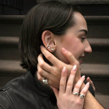 Model wearing sterling silver earrings, rings, and cuff bracelet holding the hand of a man wearing a sterling silver molten skull ring, sitting on a front stoop in Brooklyn, NY.