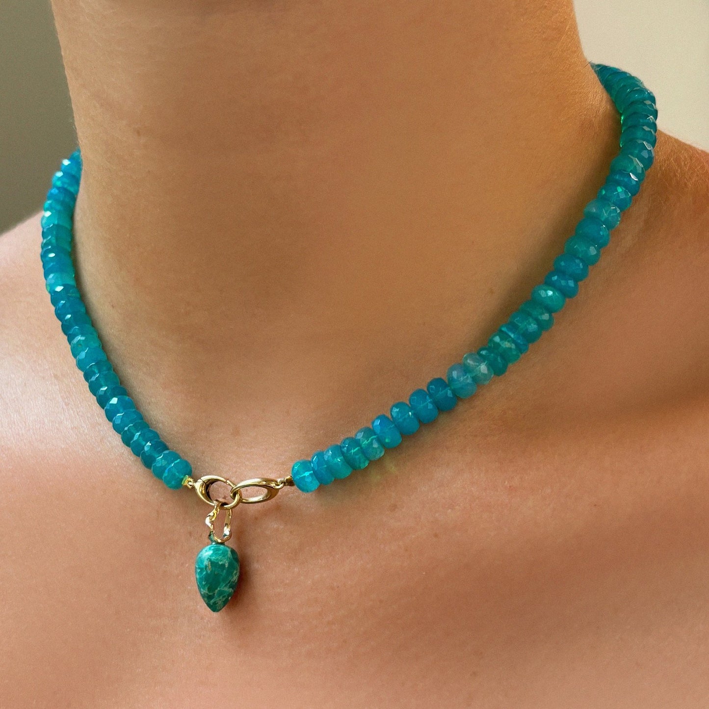 Chrysocolla acorn drop charm with flicks of teal, gold and blue with 14k gold ripple bale styled on a Blue opal necklace on a neck.