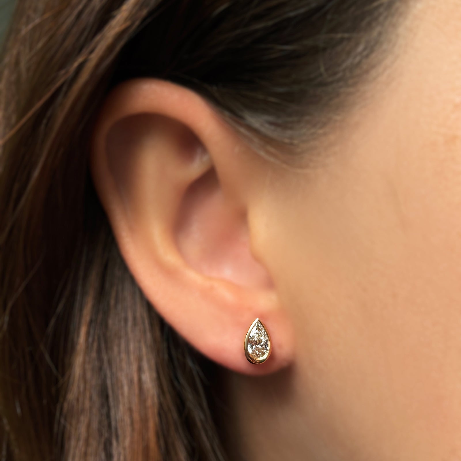 Single molten solitaire stud earring with a pear diamond in yellow gold on the ear. 