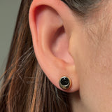 Close-up of an ear wearing a black and gold molten solitaire stud earring against a neutral background
