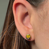 Close-up of an ear wearing a molten solitaire stud earring with citrine against a neutral background
