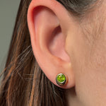 Close-up of an ear wearing a molten solitaire stud earring with peridot with a neutral background