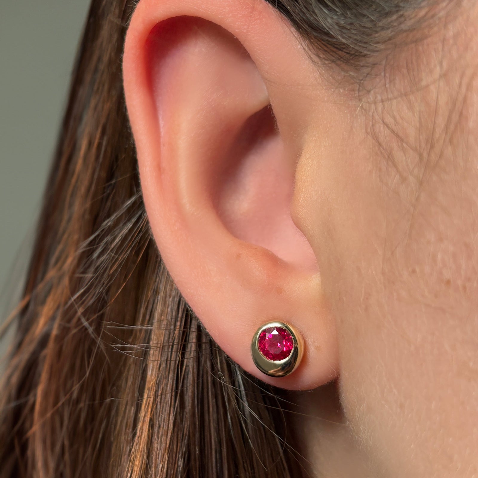 Close-up of an ear wearing a molten solitaire stud earring with ruby.
