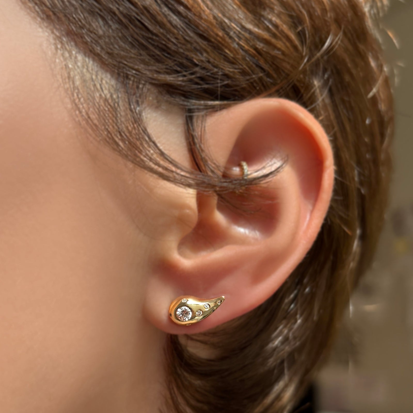 Molten stud with diamond pave on the ear of a brunette with short hair.
