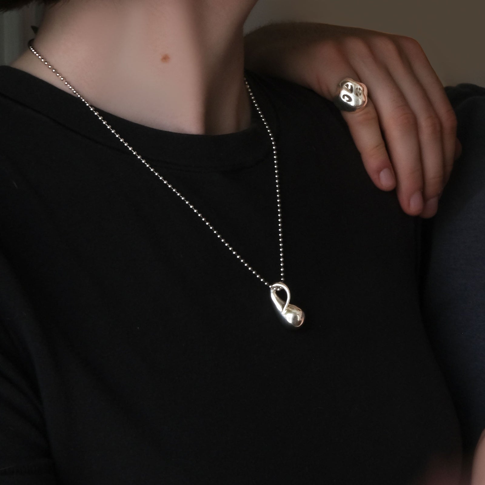 Model wearing an AMANDA PEARL sterling silver bead chain with molten drop charm, with her boyfriend's hand on her shoulder wearing a molten skull ring.