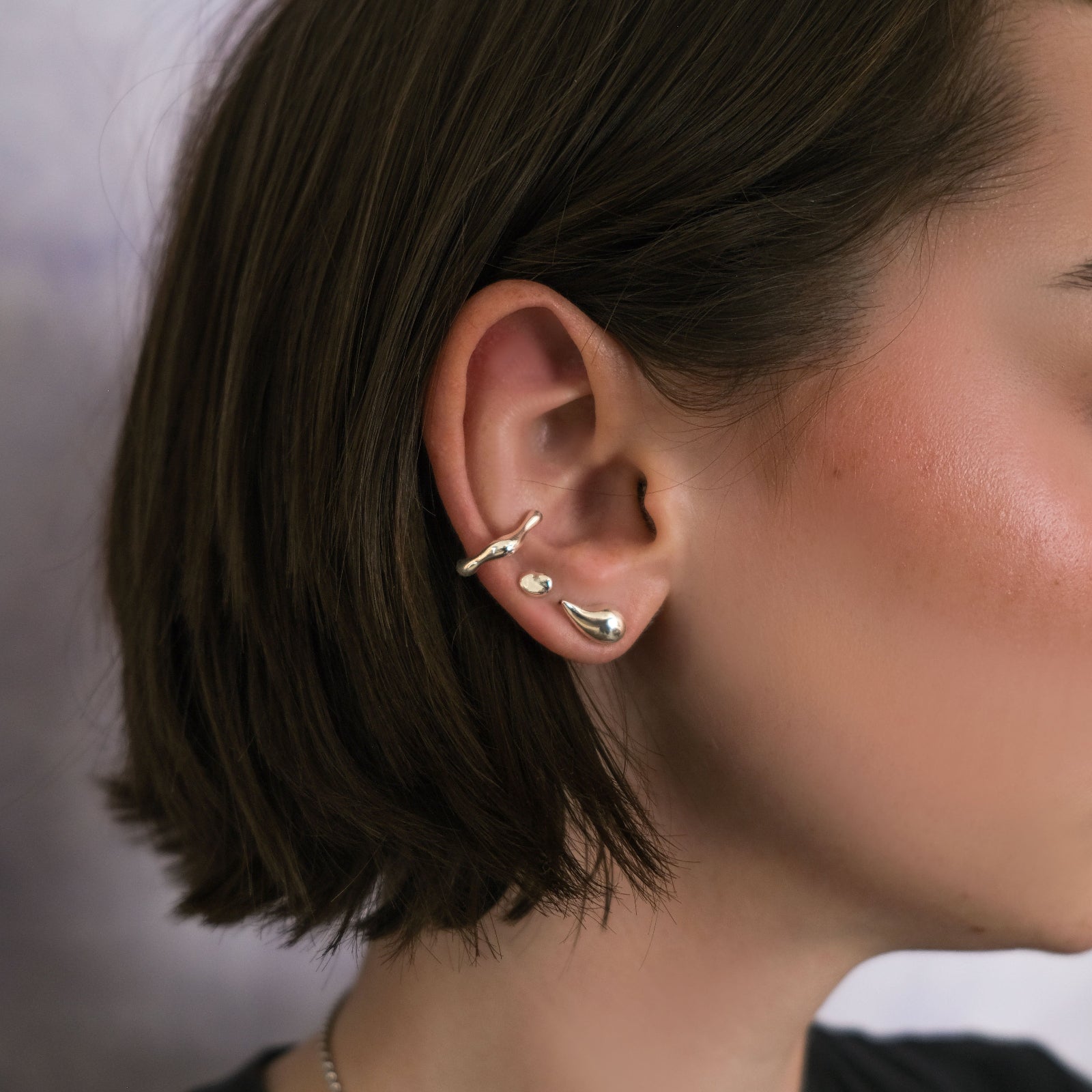 Close-up of a model wearing AMANDA PEARL recycled sterling silver earrings and ear cuff with a blurred background