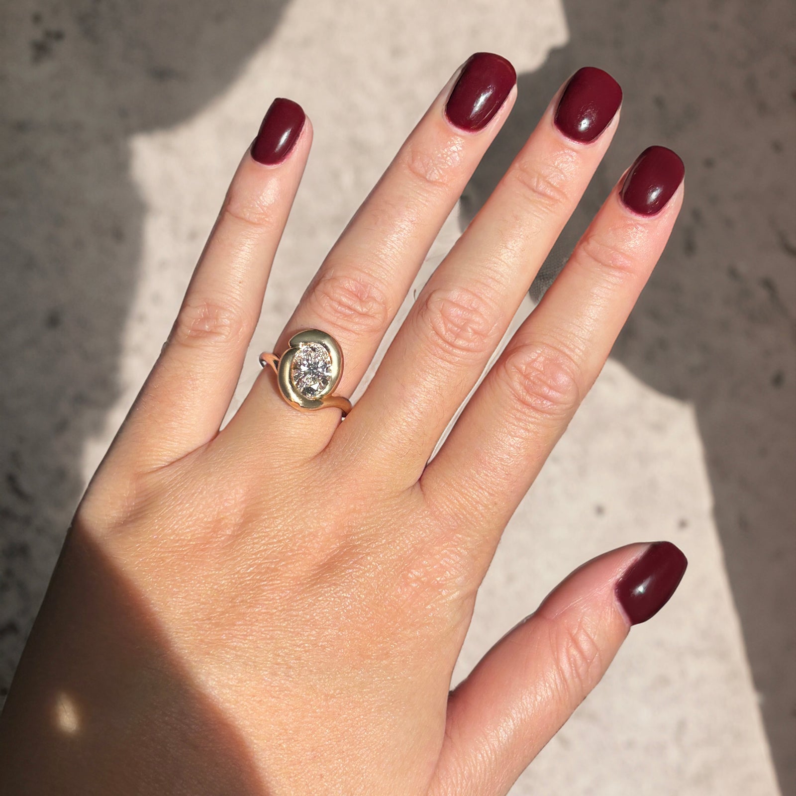 14k yellow gold molten knot ring with diamond on a model's hand with deep red nail polish.