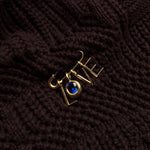 A recycled 14k gold molten safety pin iin a dark chunky knit sweater, dropping letter charms and a round molten sapphire solitaire charm spelling out LOVE.