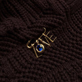 A recycled 14k gold molten safety pin iin a dark chunky knit sweater, dropping letter charms and a round molten sapphire solitaire charm spelling out LOVE.