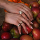 Close-up of hands with AMANDA PEARL sterling silver rings on a pile of red apples.