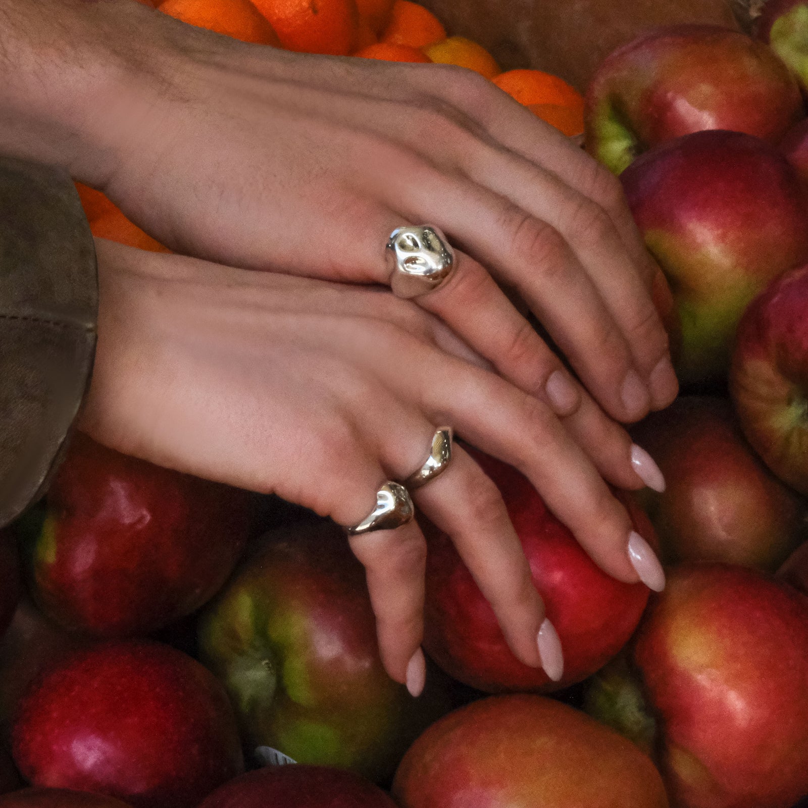Close-up of hands with AMANDA PEARL sterling silver rings on a pile of red apples.