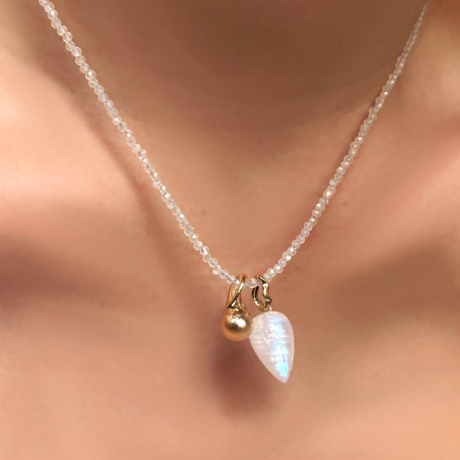 Slim gemstone necklace in moonstone with mini molten drop charm and rainbow moonstone drop charm with recycled 14k yellow gold bale hanging from a model's neck.