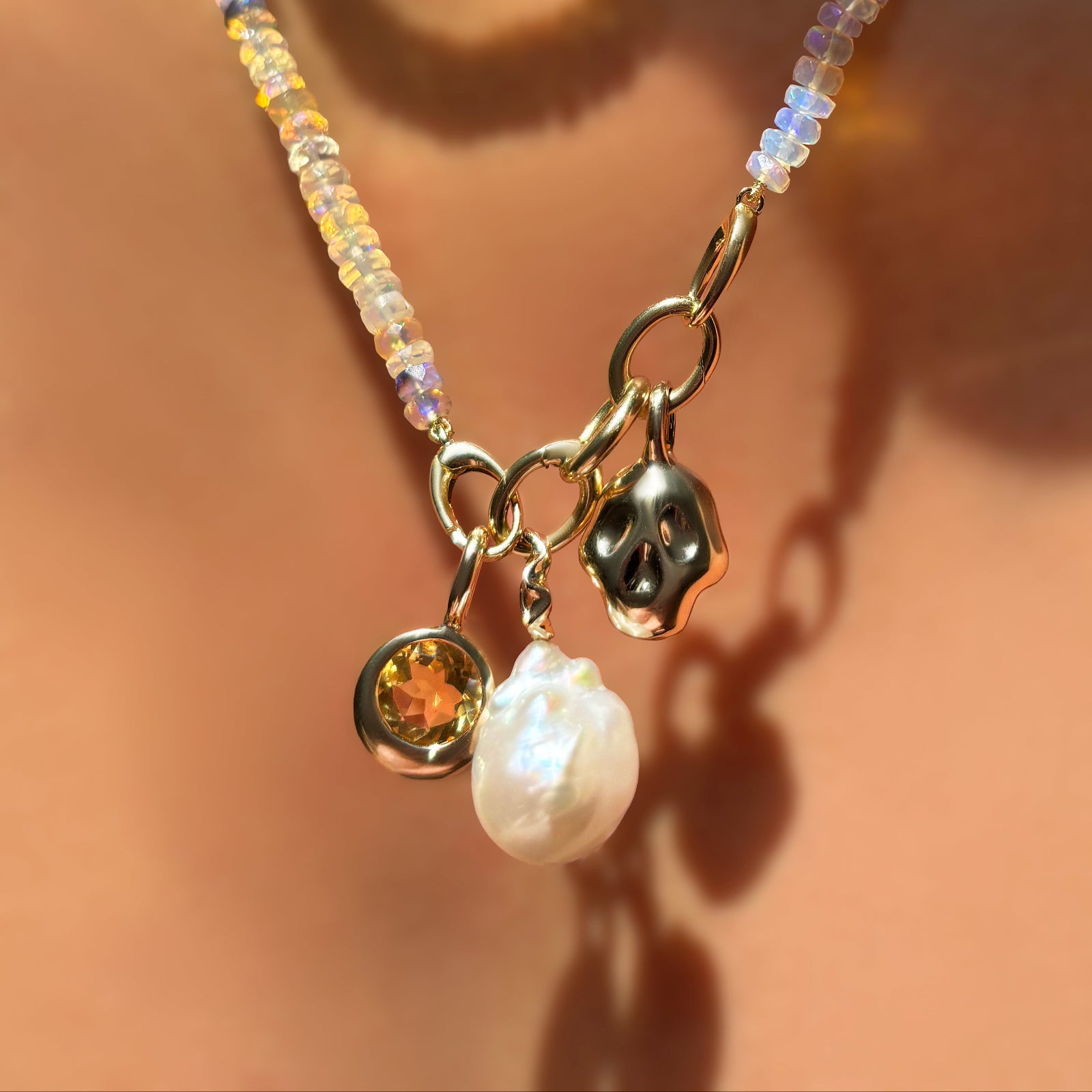 Natural multi-faceted opal necklace with triple link charm lock with molten solitaire charm with citrine, mini baroque pearl charm, and molten skull charm dangling on the neck.