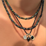 night sky faceted opal necklace layered over black spinel slim gemstone necklace holding a quill bezel charm, rutilated quartz drop charm, and black onyx molten solitaire charm on a model's neck.
