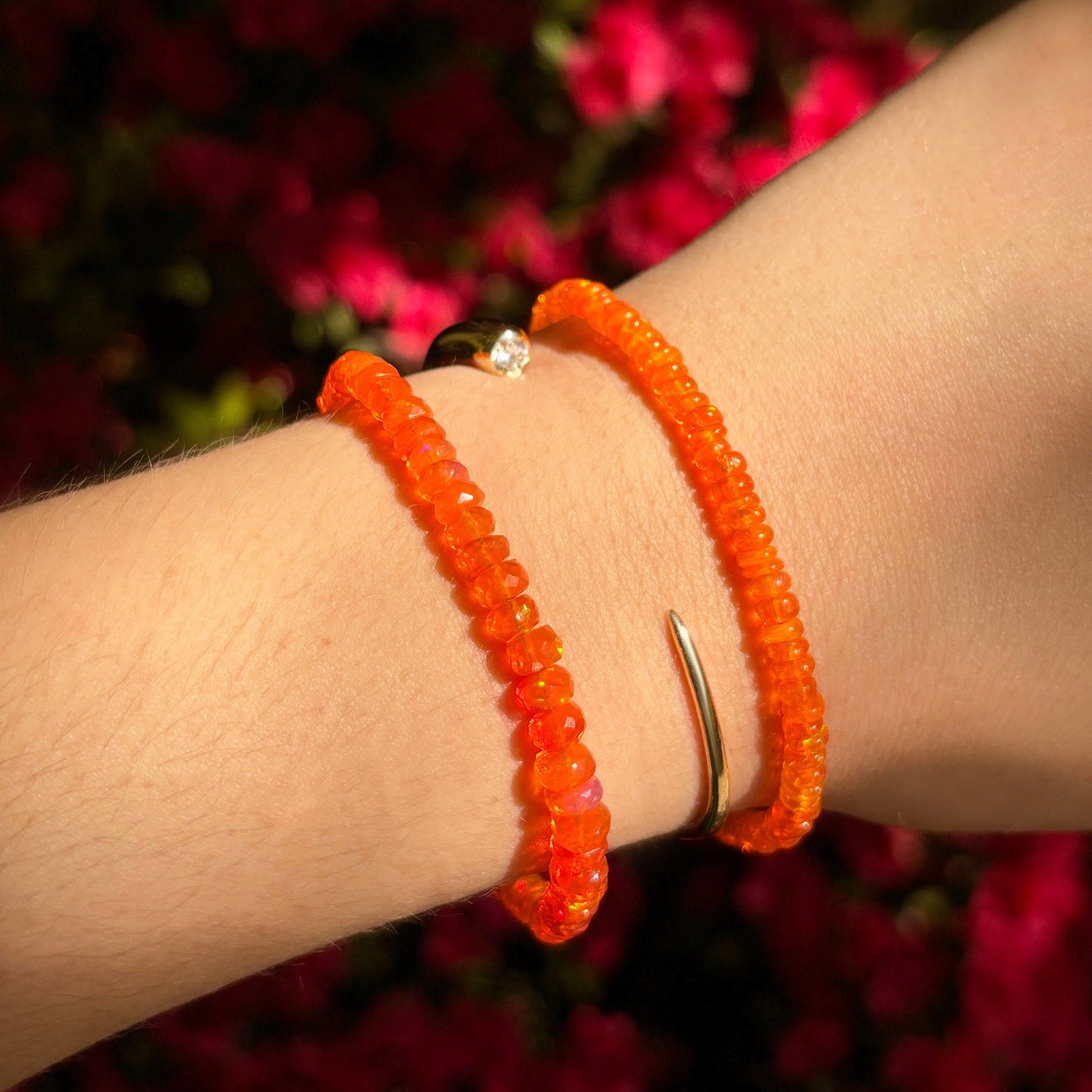 Shimmering beaded bracelet made of smooth opals in shades of bright orange on a gold linking lobster clasp styled on a wrist.
