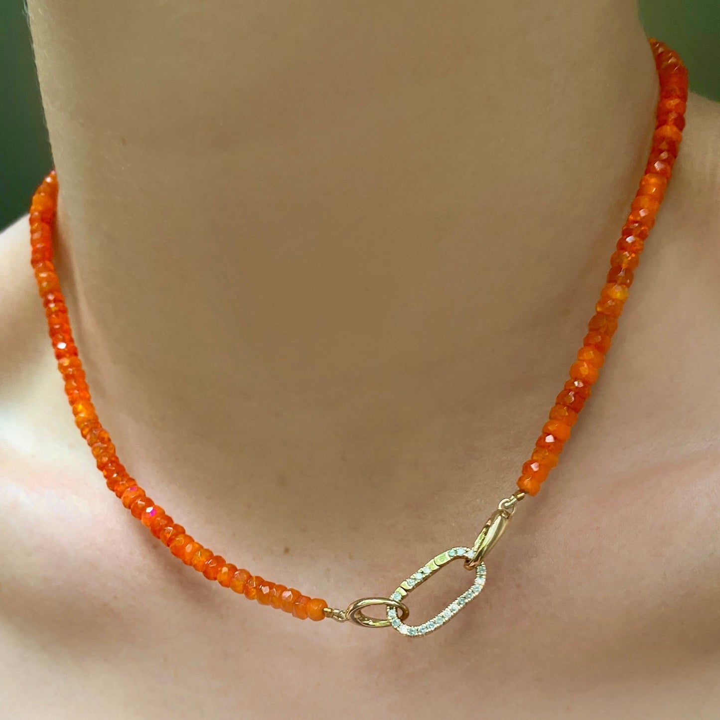 Shimmering beaded necklace made of faceted opals in shades of orange on a gold linking ovals clasp. Styled on a neck layered with a medium pave face charm lock.