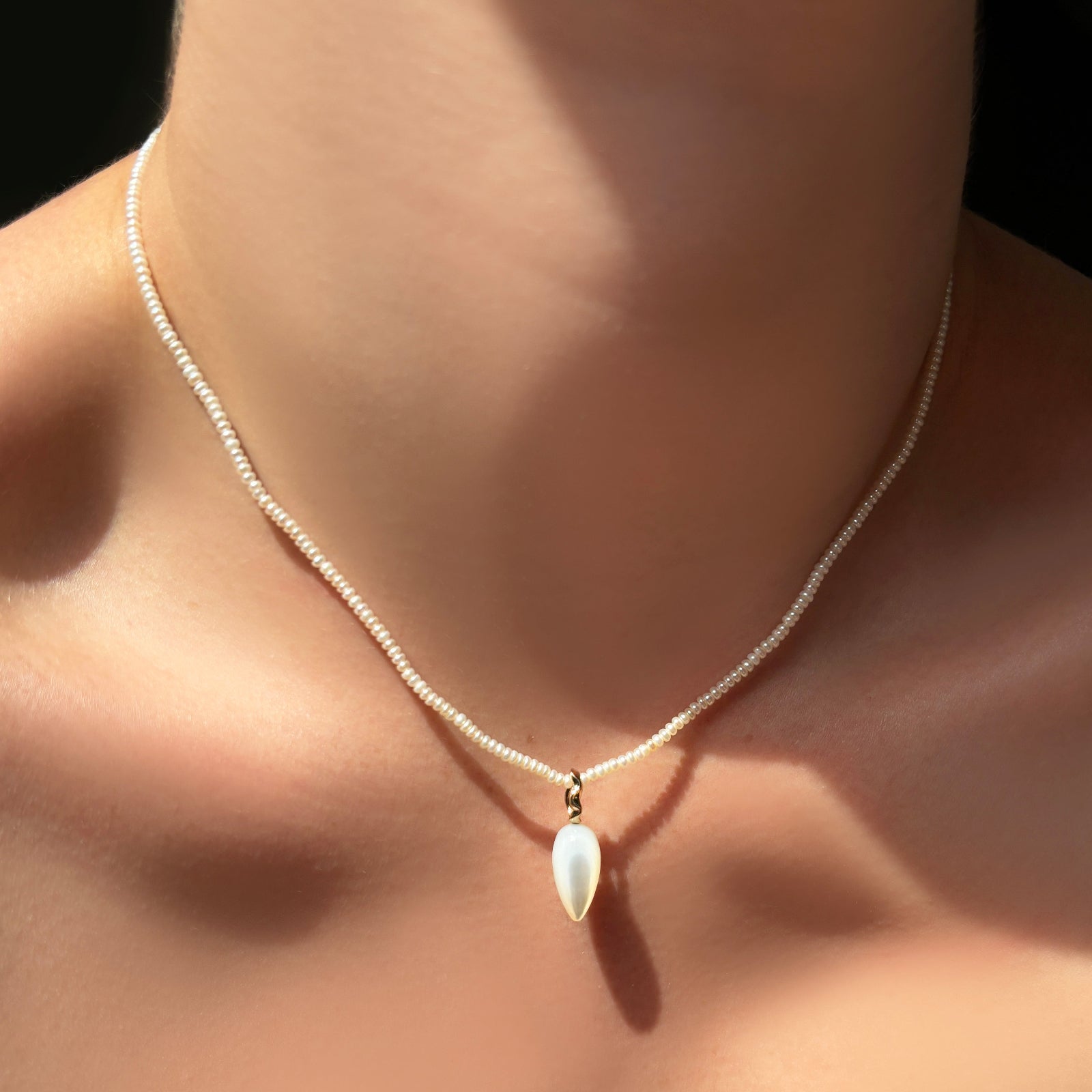 Pearl slim gemstone necklace with a mother of pearl drop charm on the neck.