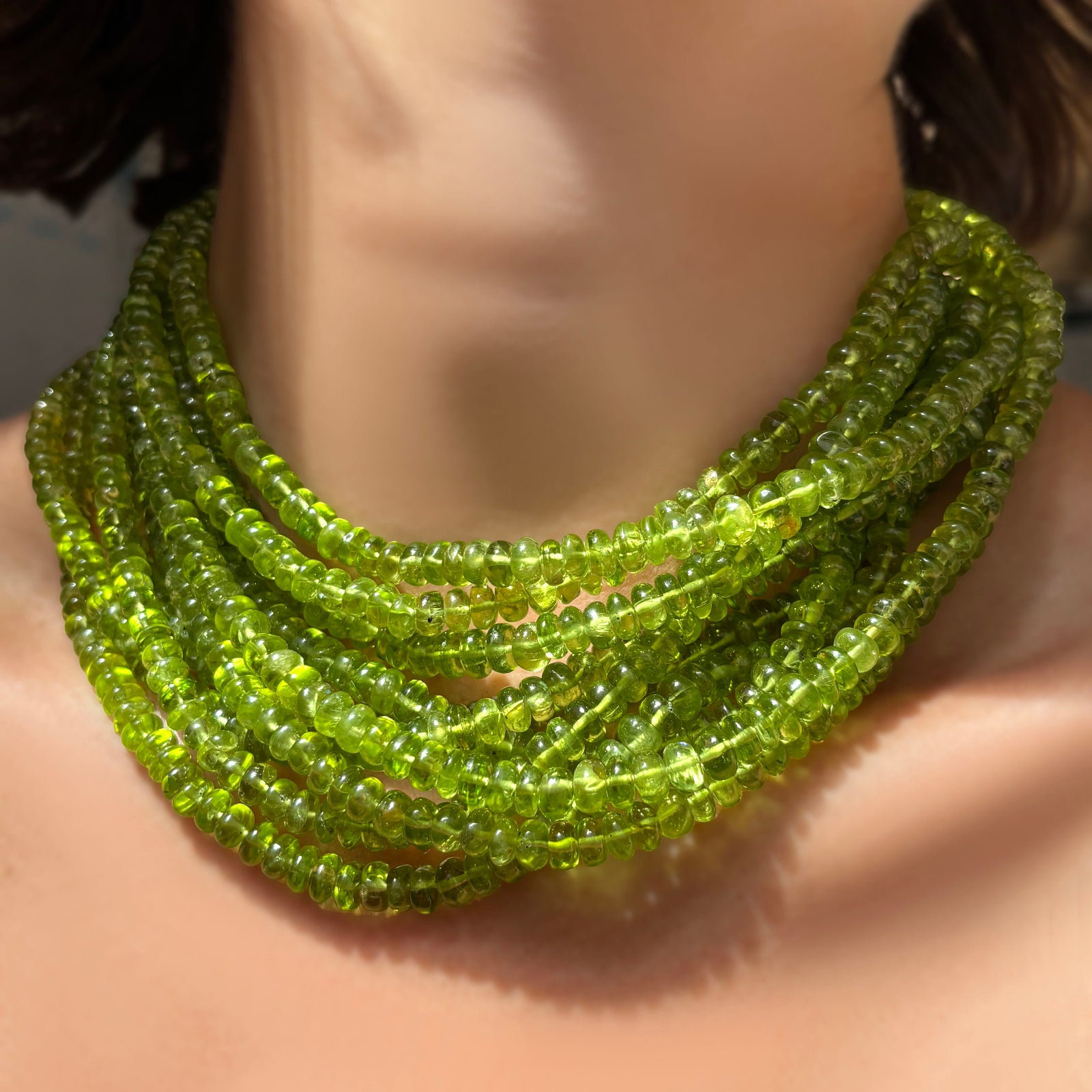 A stack of AMANDA PEARL peridot rondelle necklaces on a model's neck.
