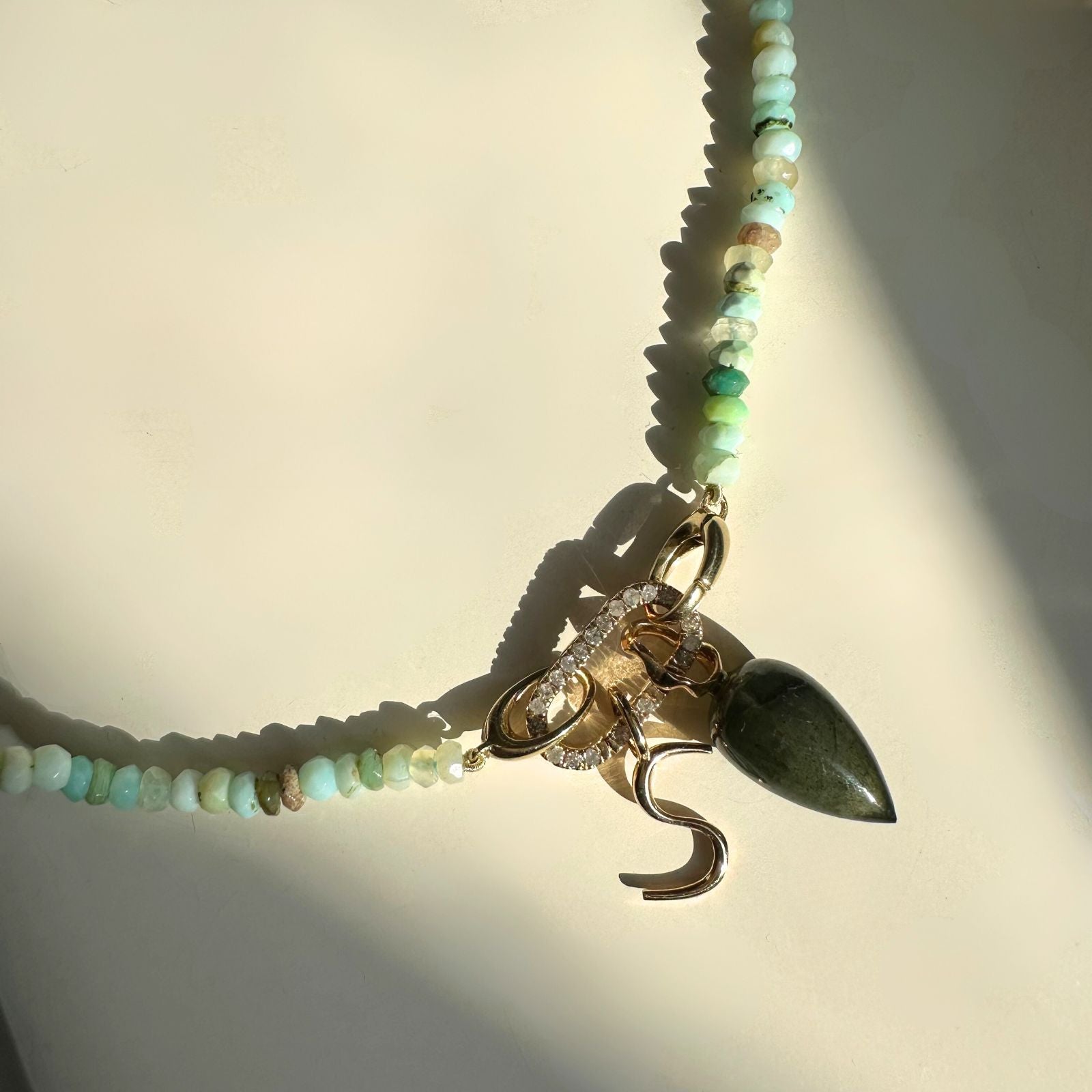 Peruvian faceted opal necklace with pavé face charm lock dropping an "S" letter charm and labradorite drop charm on a white background.