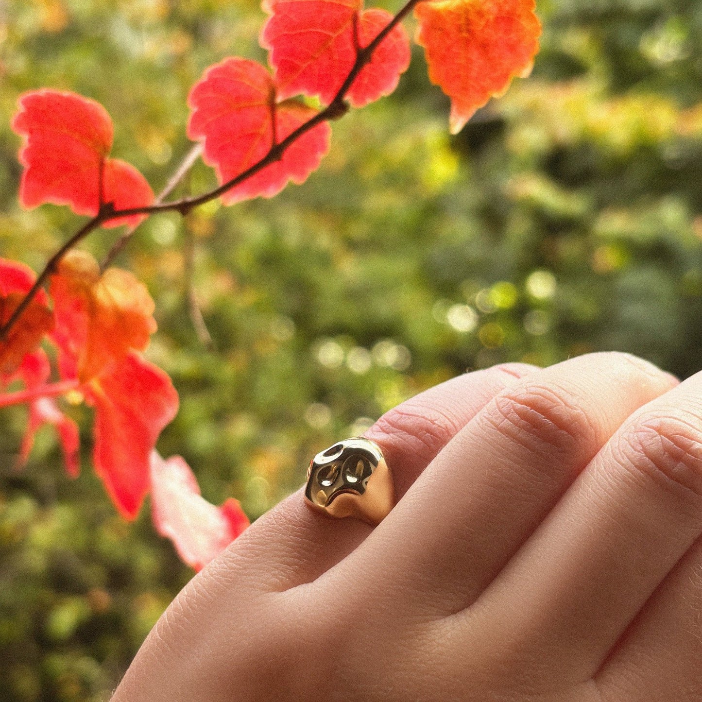 14K recycled Yellow Gold skull pinky ring styled on a hand, with fall leaves in the distance