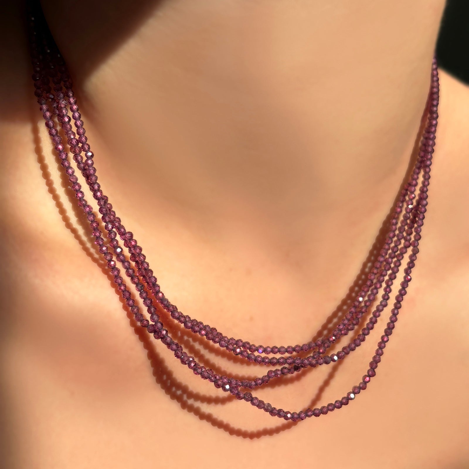 Multiple purple garnet slim gemstone necklaces layered on a model's neck.