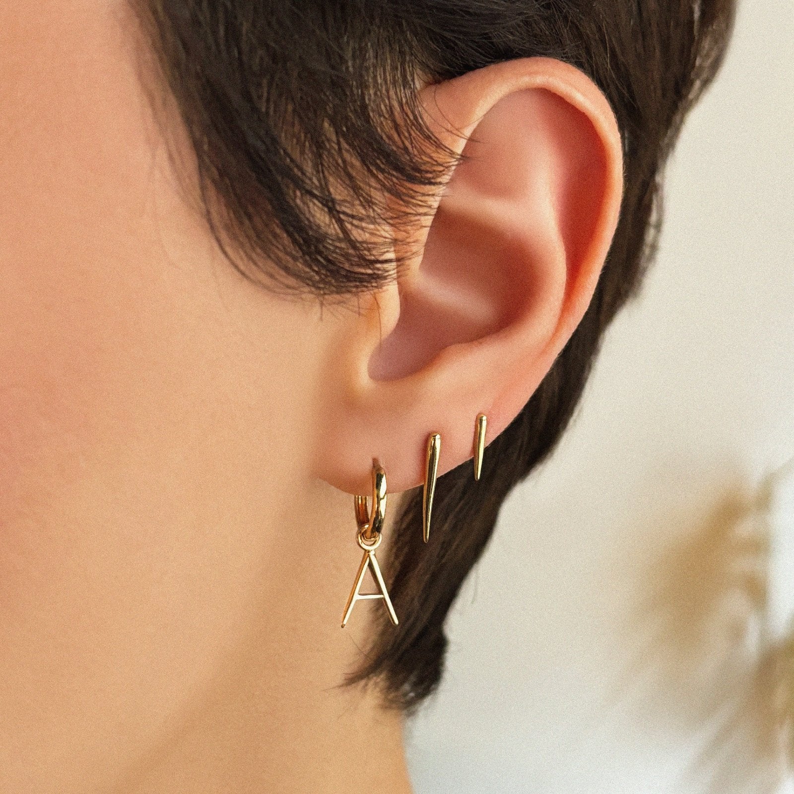 14k gold Letter "A" Huggie styled on an ear with our Medium and Small Quill Spike Studs.