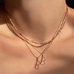 red pink faceted spinel layered with a diamond cut bead chain with a letter "B" charm on a model's neck.