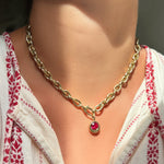 Necklace with a ruby solitaire charm worn by a person in a white and red patterned top.
