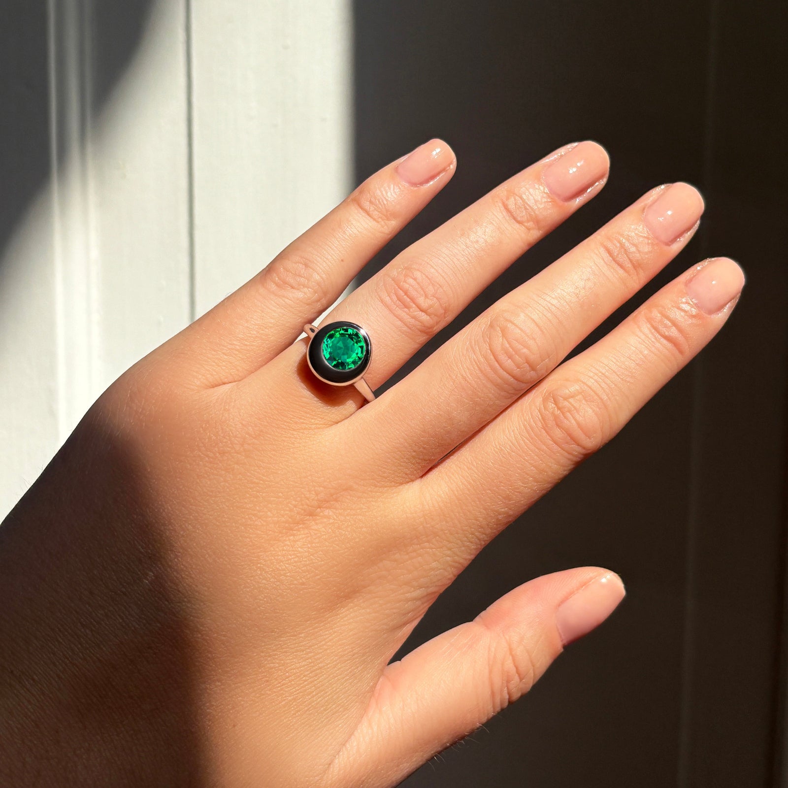 AMANDA PEARL Molten solitaire ring in recycled 14k gold with a cultivated emerald center stone on a model's hand.