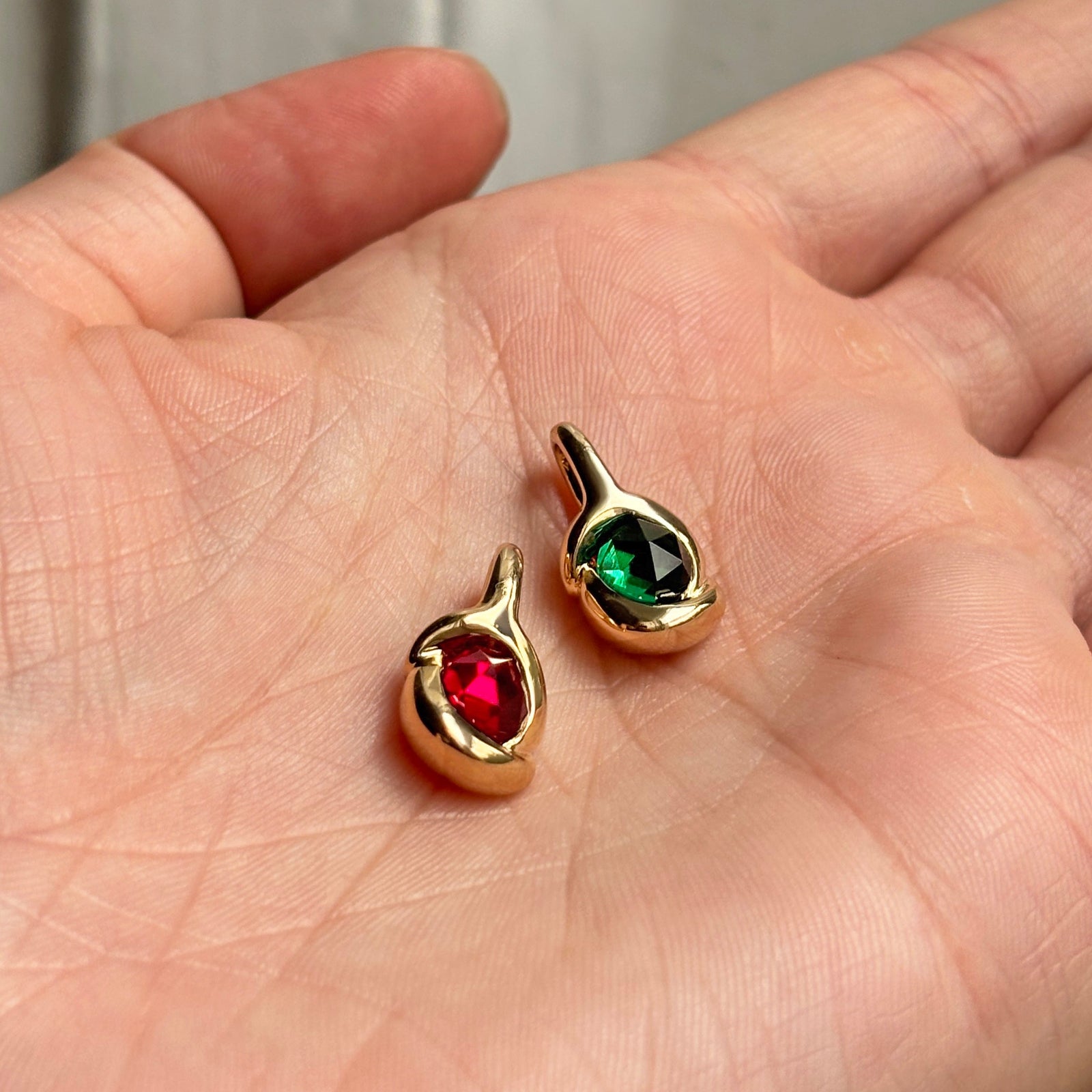 Ruby and emerald round rose cut gemstone knot charms in recycled 14k yellow gold sitting in a hand.