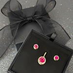 A ruby molten solitaire bundle, comprised of molten stud earrings and a molten solitaire charm, both cast in 14K recycled yellow gold, is boxed with black organza ribbon.