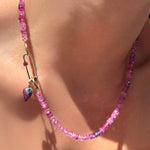 Fuchsia faceted sapphire necklace with paperclip charm lock with ruby hanging a ruby zoisite drop charm on yellow gold ripple bale on a model's neck.