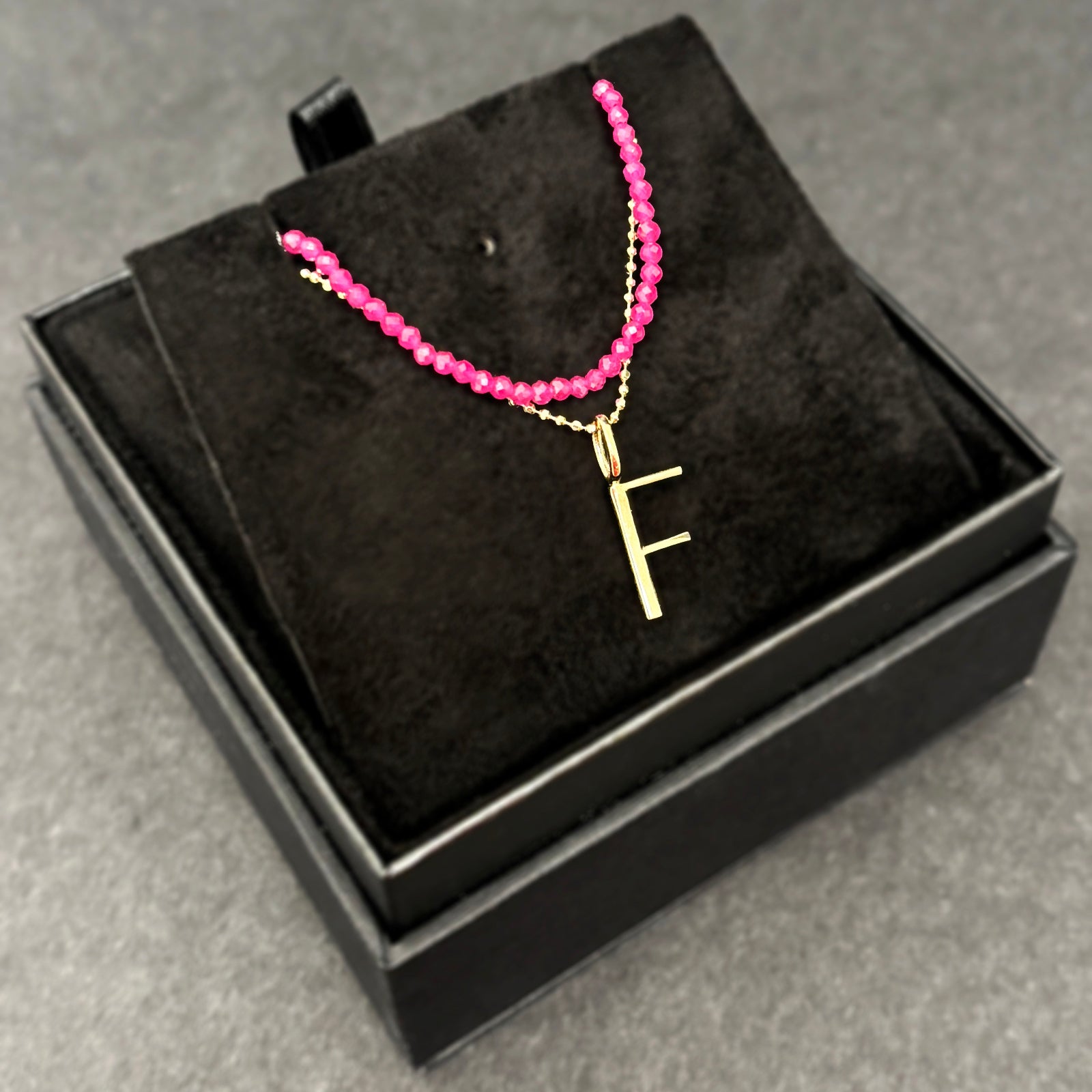 Ruby slim gemstone necklace with diamond cut bead chain with letter F charm bundled in a black jewelry box.