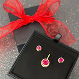 A black gift box with a pair of molten solitaire studs with round rubies and a molten solitaire charm with a round ruby.