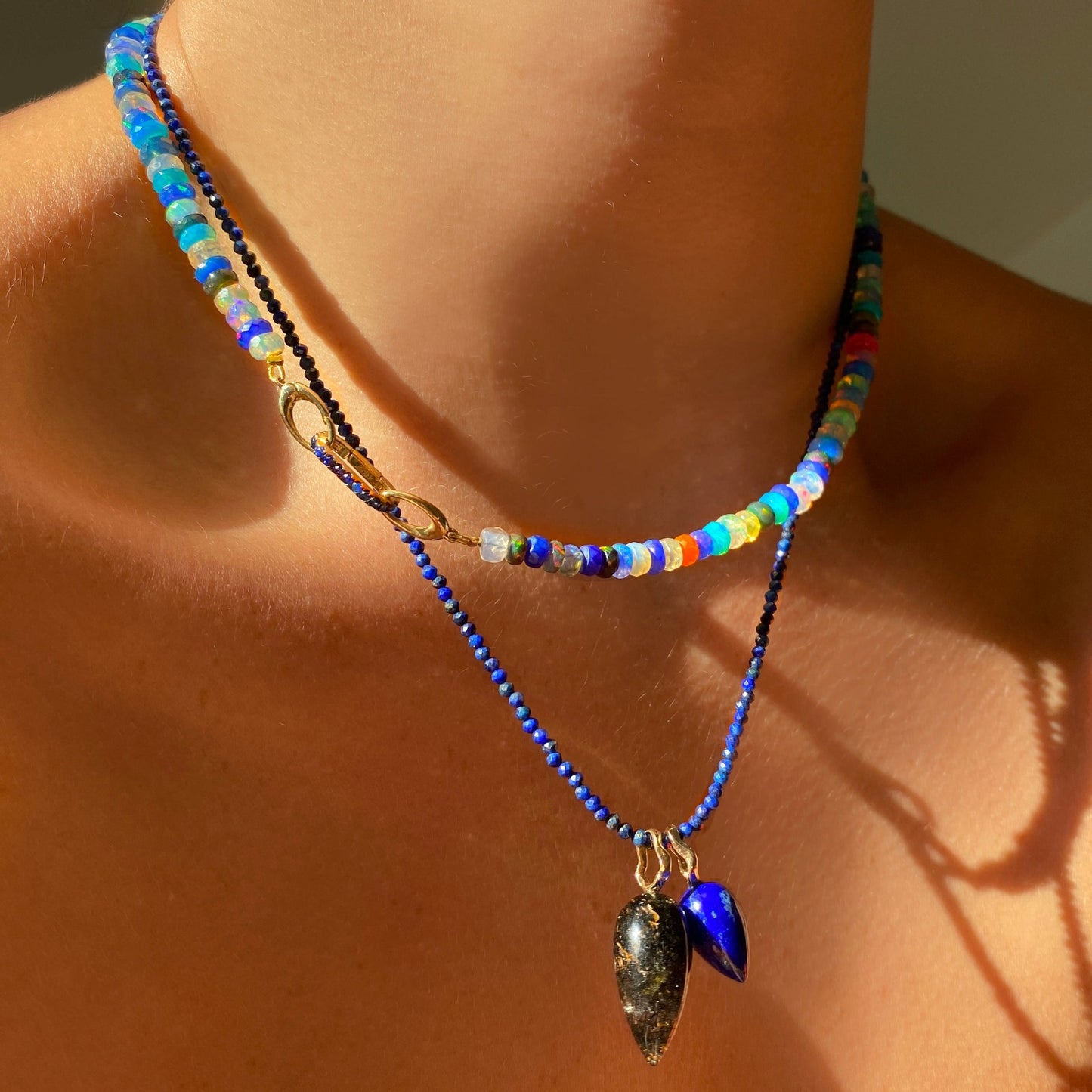 Shimmering beaded necklace made of 2mm faceted opals in shades of blue on a gold linking lobster clasp. Styled on a neck layered with two acorn charm locks.