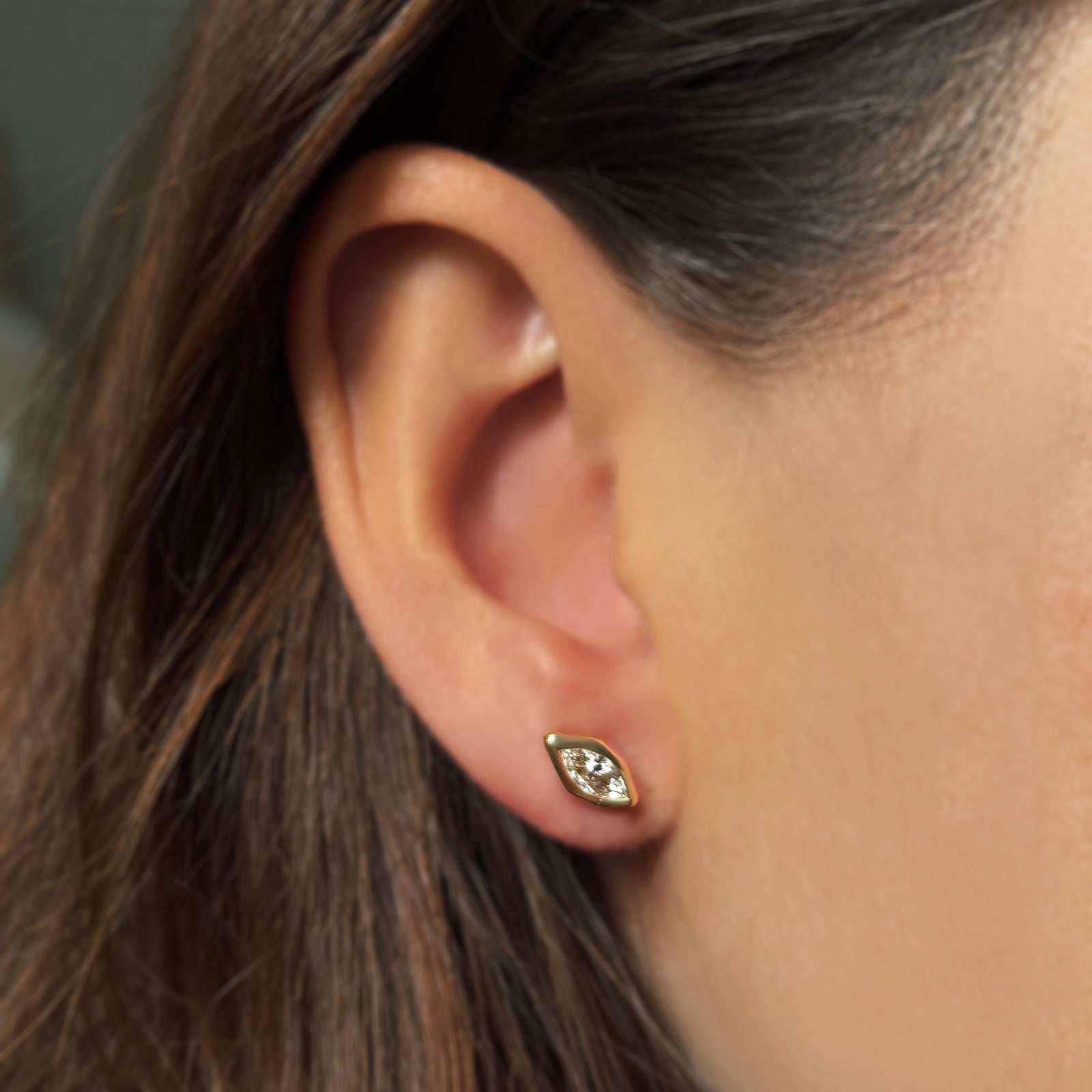 Single molten solitaire stud earring with a marquise diamond in yellow gold on the ear. 