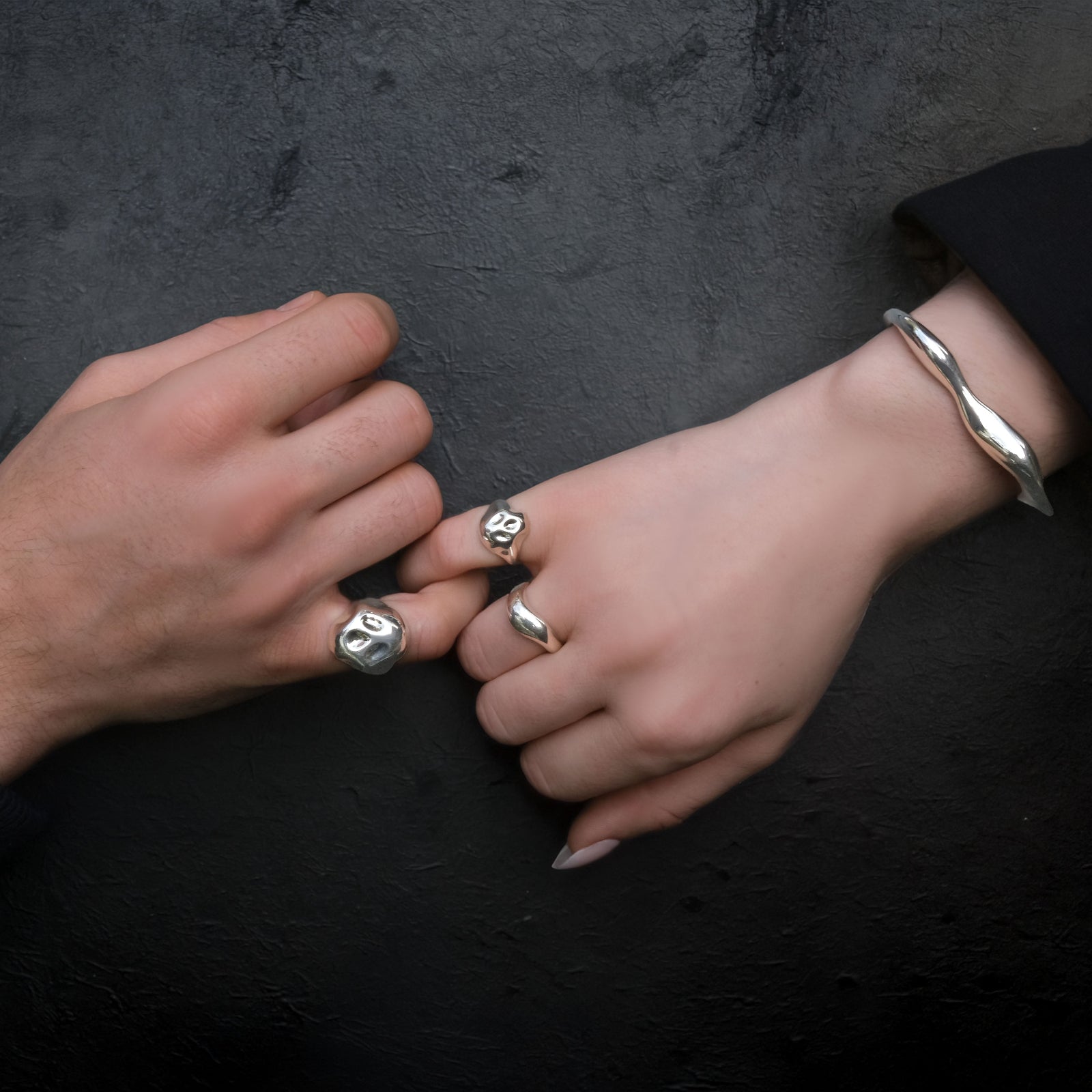 Two hands clasping pinkies wearing AMANDA PEARL sterling silver jewelry against a dark background.