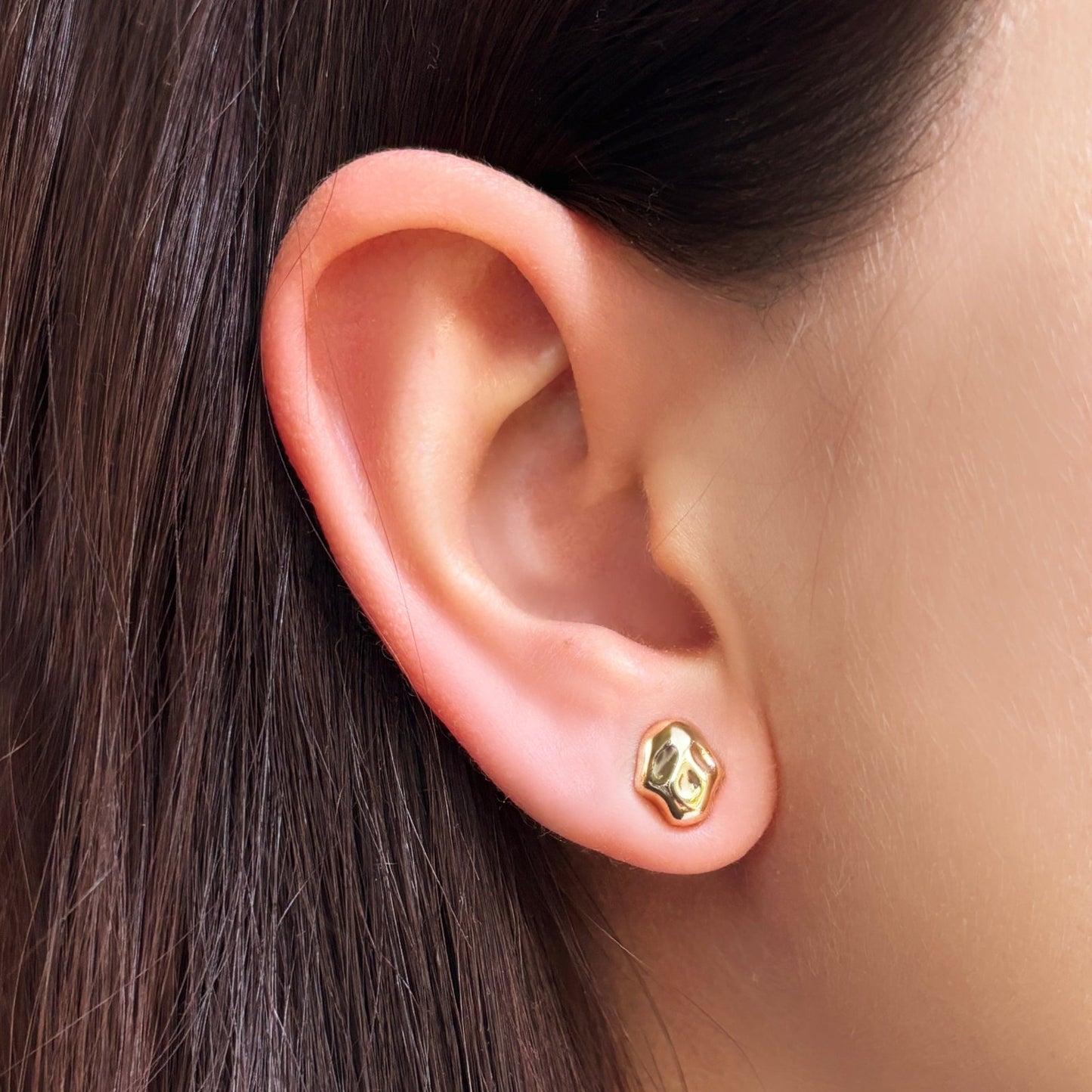 14k recycled gold skull studs on an ear