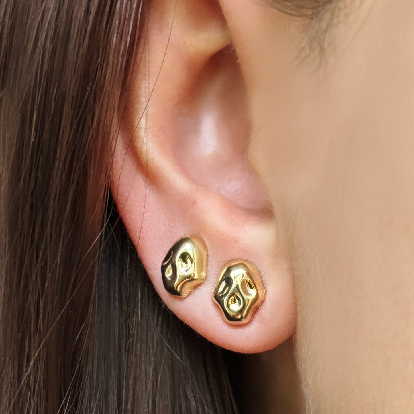 14k recycled gold skull studs on an ear