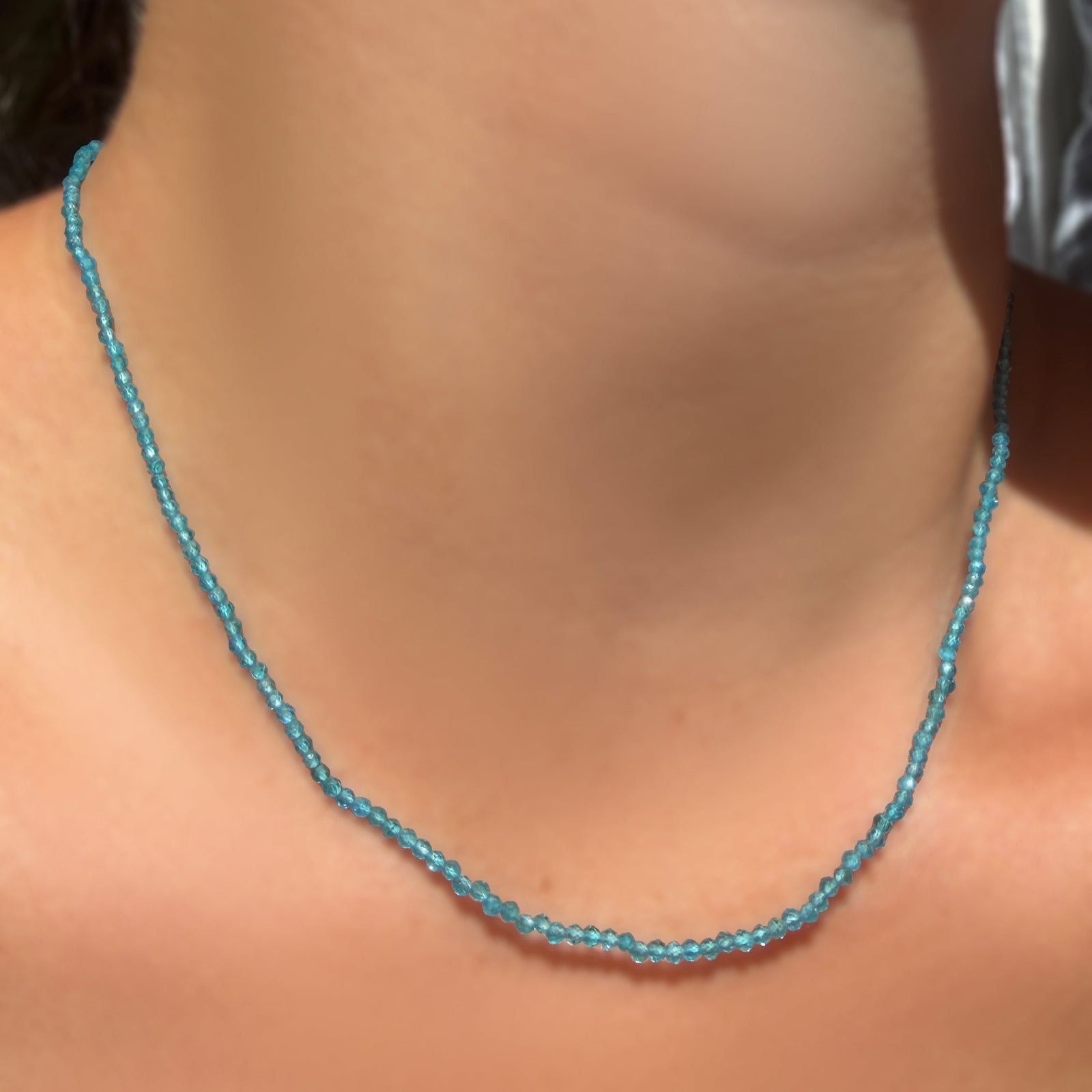 AMANDA PEARL Slim Gemstone Necklace with 2mm faceted apatite beads on a recycled gold lobster clasp with extender chain on a model's neck.