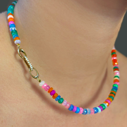 Shimmering beaded necklace made of faceted opals in shades of fiery blues, yellows, teal, and purple on a gold linking ovals clasp. Styled on a neck layered with a small diamond charm lock.