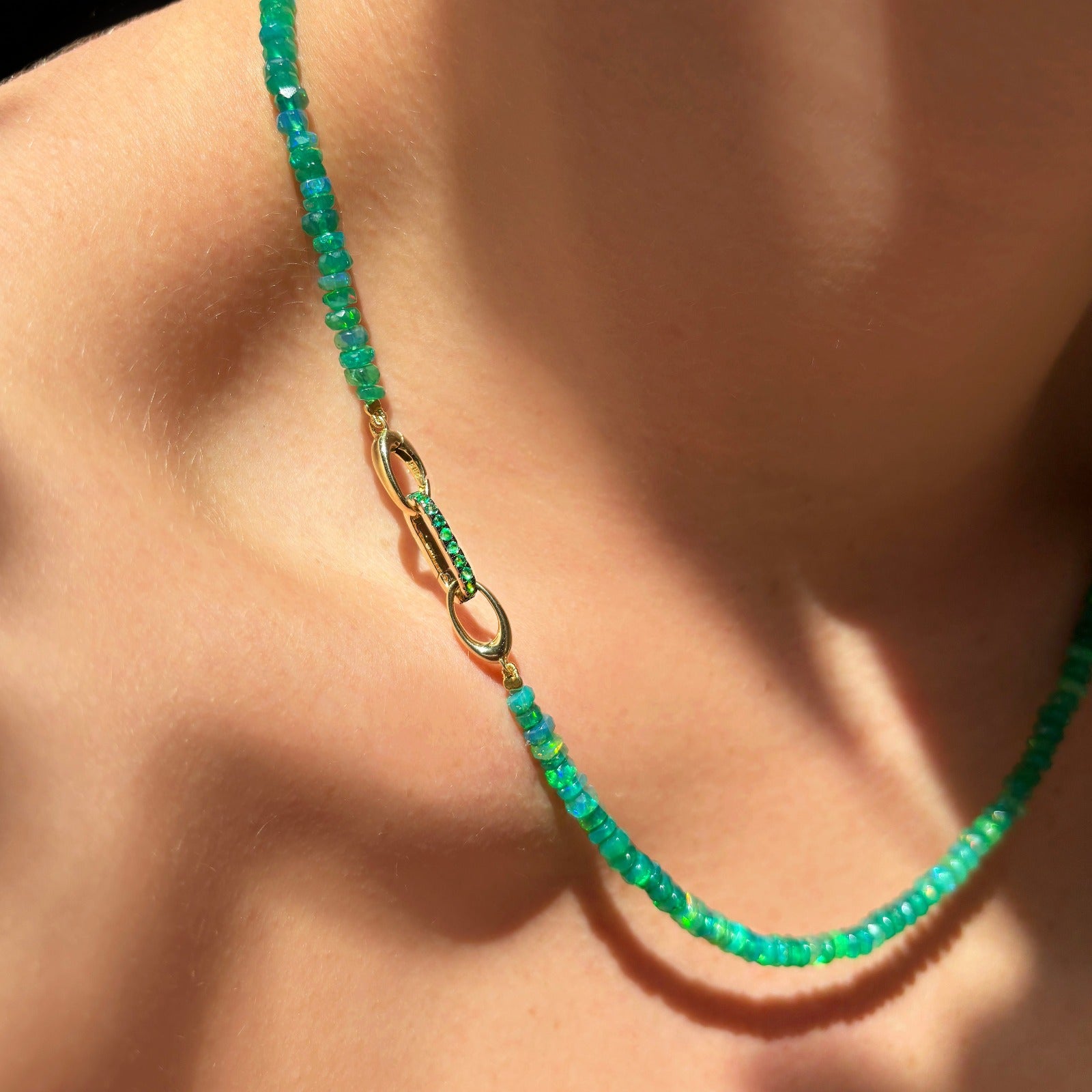 14k yellow gold oval locking charm with green stones styled on a neck locked onto oval clasps of a beaded necklace.