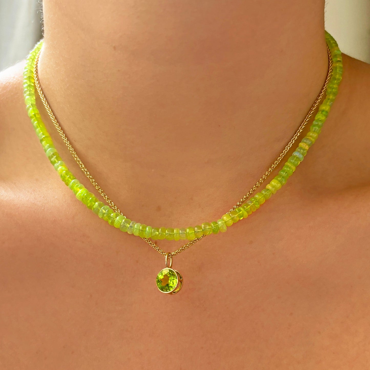 Shimmering beaded necklace made of smooth opal rondels in shades of yellow-green on a slim gold lobster clasp. Styled on a neck layered with the wheat chain necklace and round solitaire charm.