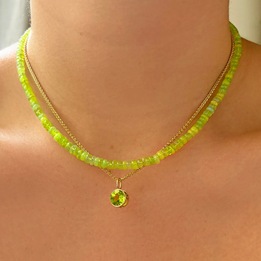 14k gold Peridot Round Solitaire Charm. Styled on a neck hanging from a wheat chain necklace. 