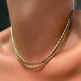 A 14k gold sprinkle chain layered with a tibet chain necklace on a model's neck.