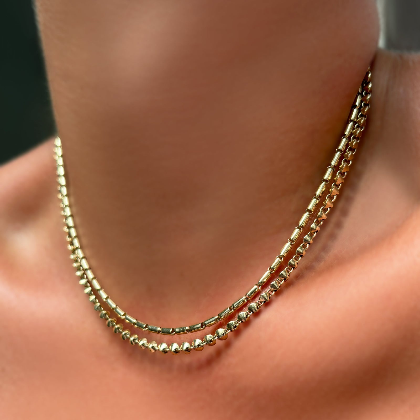 A 14k gold sprinkle chain layered with a tibet chain necklace on a model's neck.