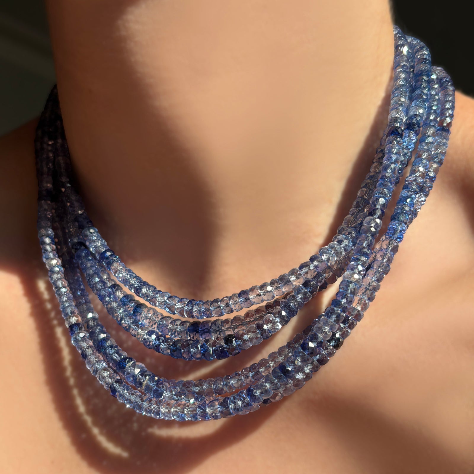 Stack of denim blue faceted sapphire necklaces on a model's neck.