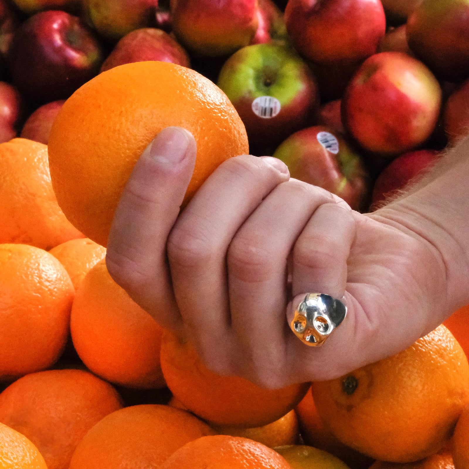 Model wearing an AMANDA PEARL recycled sterling silver Molten Skull Ring while picking out oranges.
