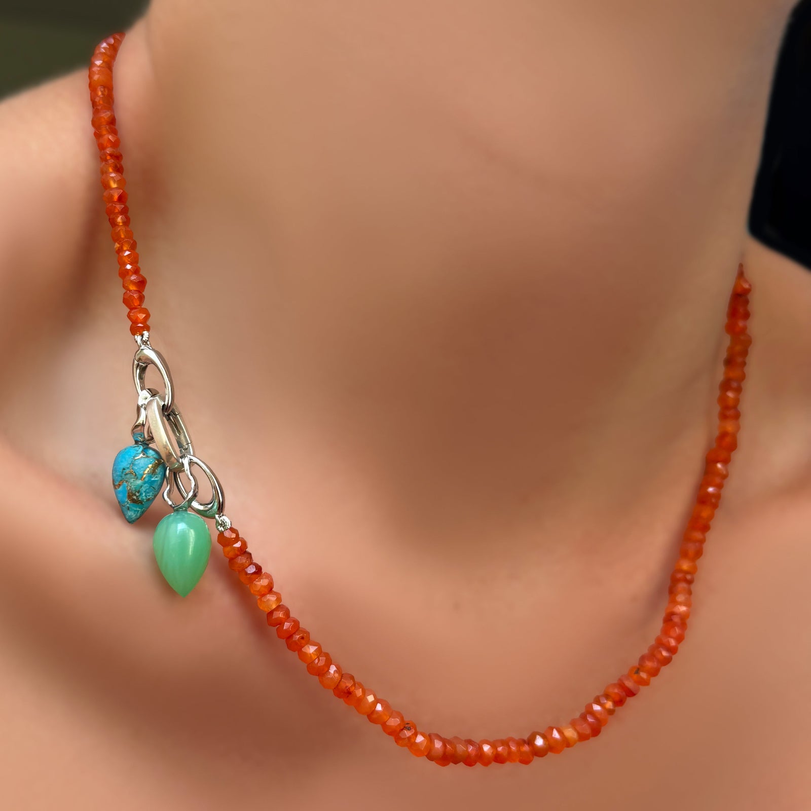 AMANDA PEARL faceted carnelian necklace with recycled sterling silver evolution clasp holding a small oval charm lock with turquoise and chrysoprase drop charm with recycled sterling silver ripple bales on a model's neck.